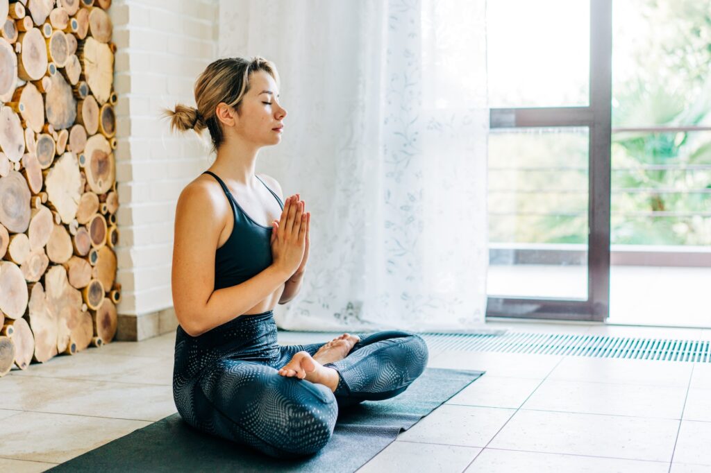 Young concentrated woman meditates at home after yoga. Mindful lifestyle, care of body and mind.